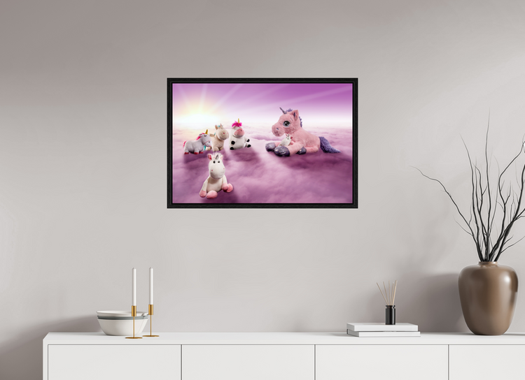 In einem neutralen hellbraunen Raum hängt ein Bild an der Wand, auf dem sich sechs Einhörner auf rosafarbenen Wolken versammelt haben. Im Hintergrund steht die Sonne am Horizont. Hab einen schönen Tag.